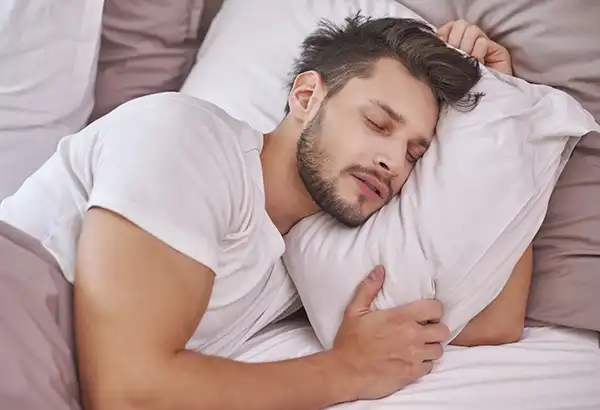 Hombre durmiendo plácidamente abrazado a su almohada, disfrutando de los beneficios de un suplemento natural para el insomnio crónico.