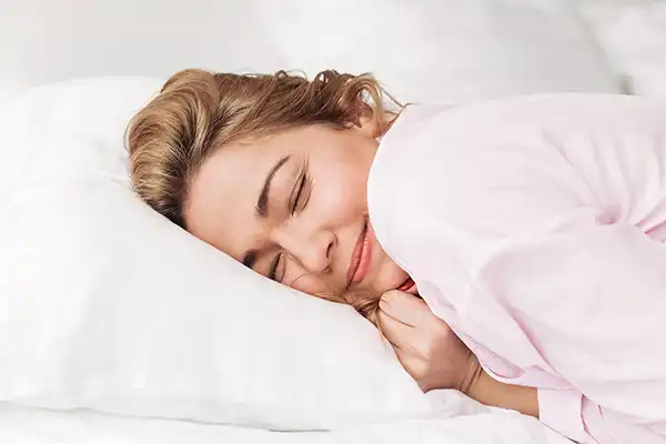 Mujer durmiendo plácidamente de lado sobre una almohada blanca, reflejando un descanso profundo y reparador con Sanasueño.